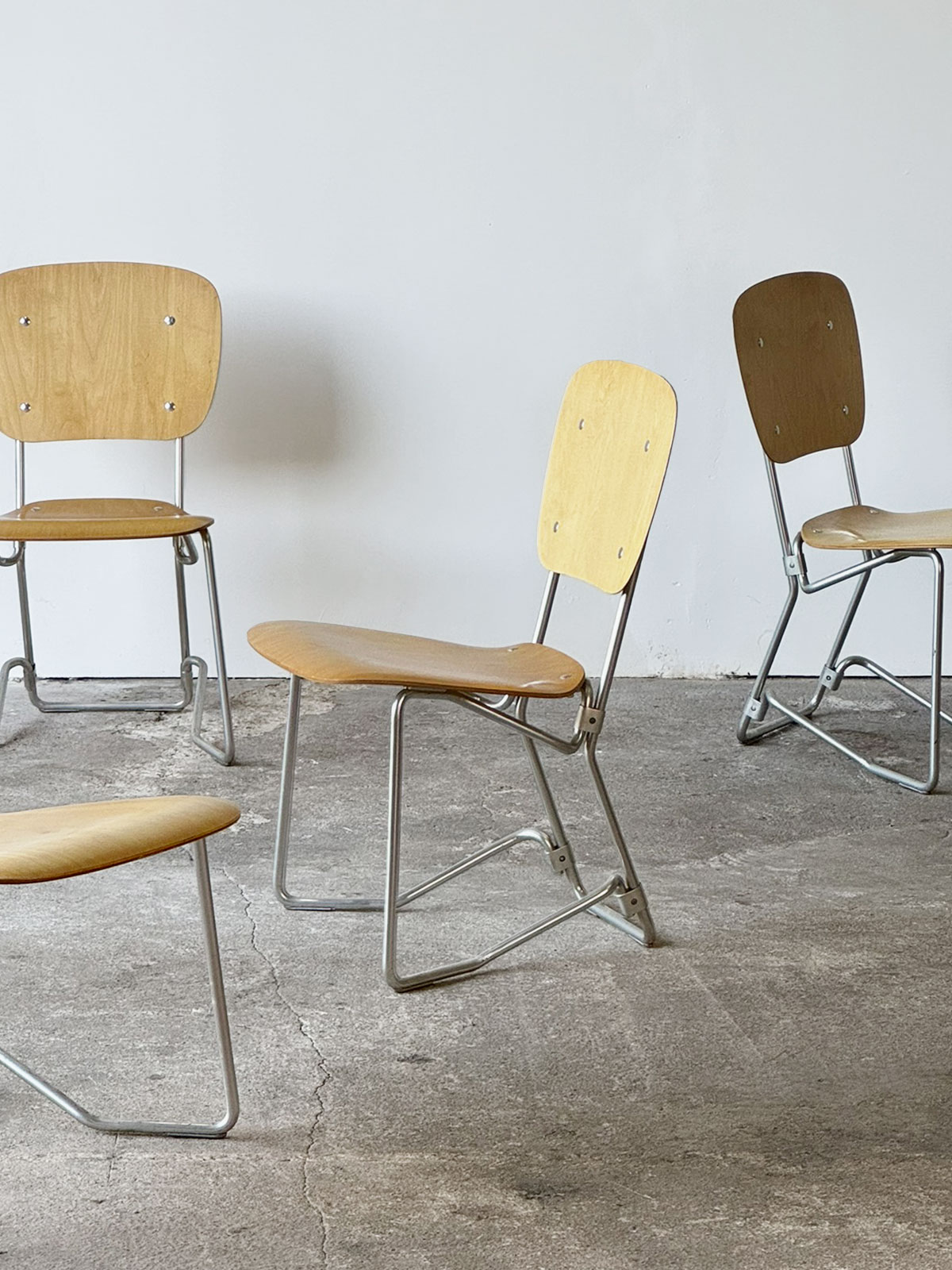 Cztery krzesła Aluflex ustawione w pełnej perspektywie, z widocznymi aluminiowymi ramami i sklejką bukową.