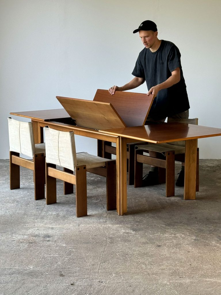 Stół Mou w trakcie rozkładania, otoczony czterema krzesłami Monk, widok w pełnej perspektywie.