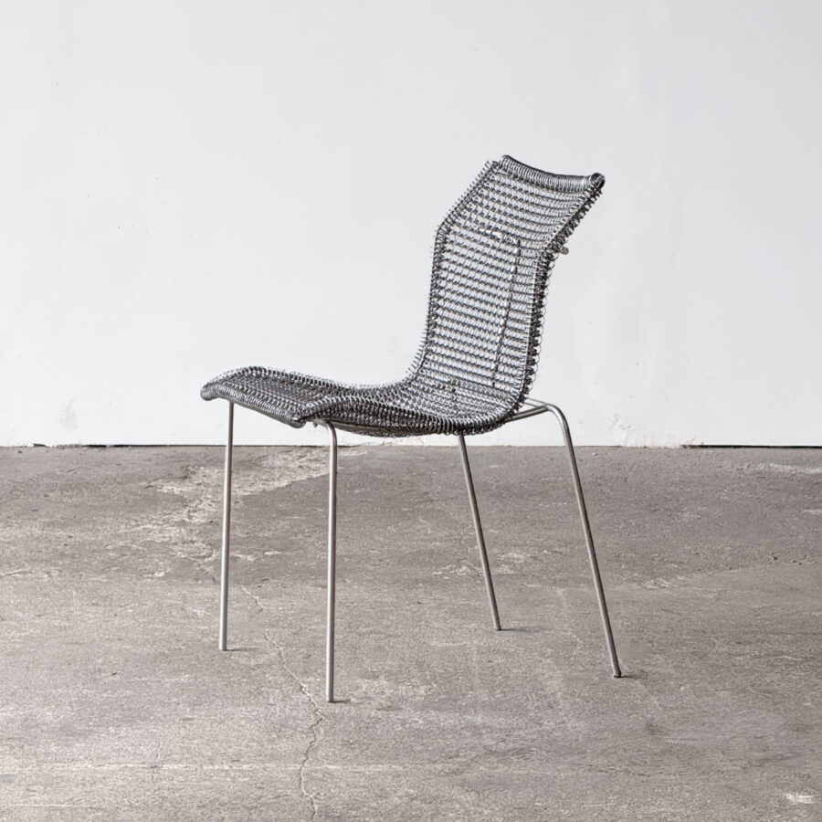 Widok frontowy krzesła Rascall, zaprojektowanego przez Nialla O'Flynn'a i wyprodukowanego przez Spectrum w latach 1997–2001. Cienka stalowa konstrukcja z siedziskiem wyplecionym ze sprężyn galwanizowanych.